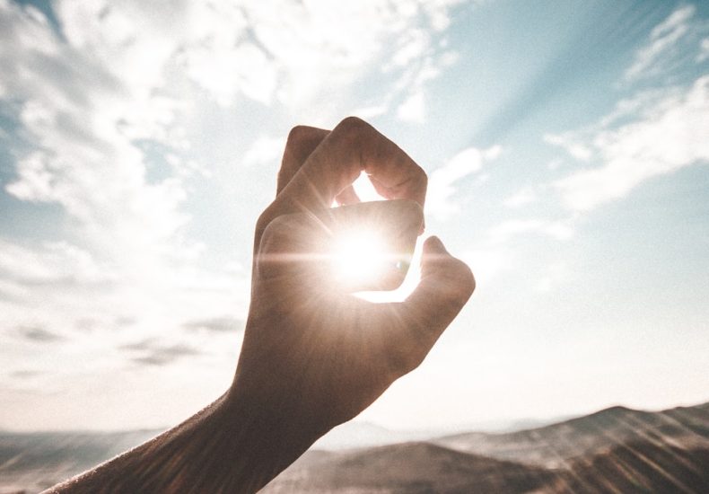 photography of sun glaring through the hole of finger