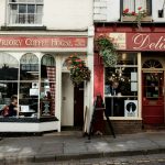 the front of a coffee shop with a woman sitting in the window